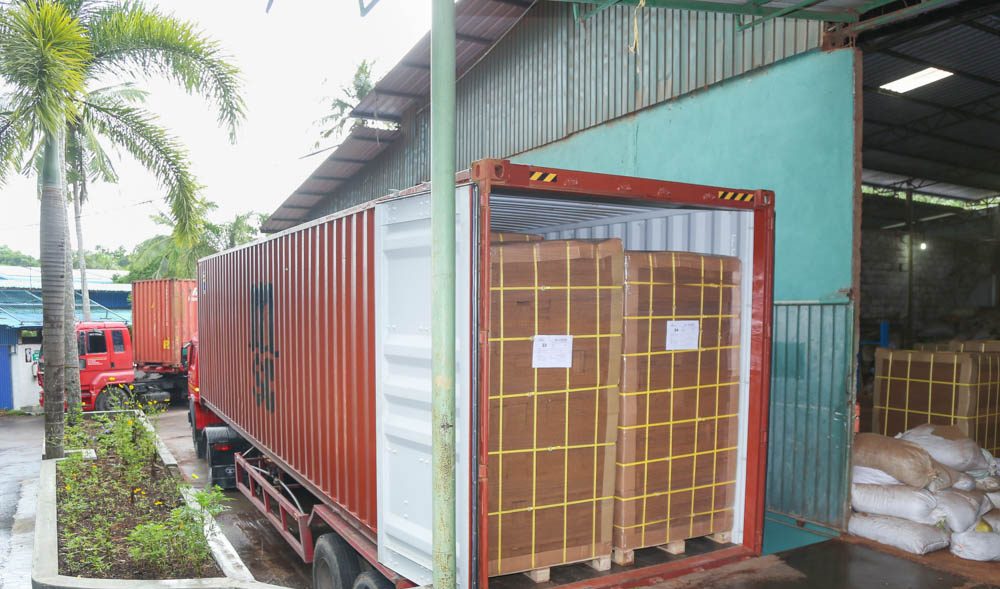 A shipping container backed onto a factory loading bay, part loaded with pallets of coco peat blocks