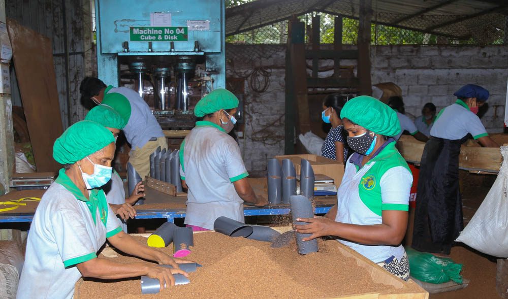 Workers forming coir cubes at a press on the factory floor